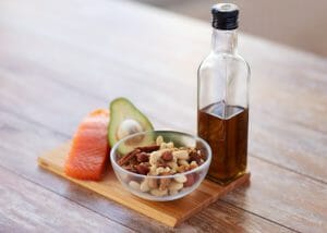 a portion of fresh salmon, half an avocado, nuts in a bowl and olive oil on a wooden board