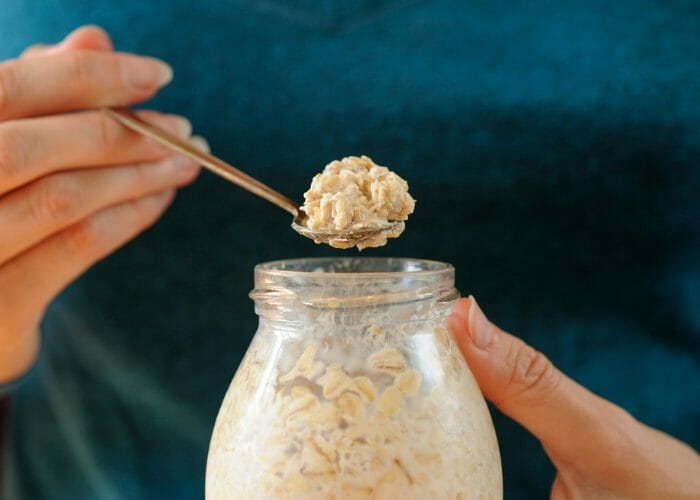 woman holding up a spoonful of overnight oats from a jar