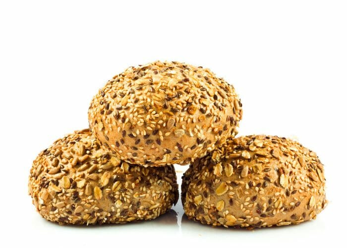 Round protein bread buns with seeds and grains on a white surface and white background