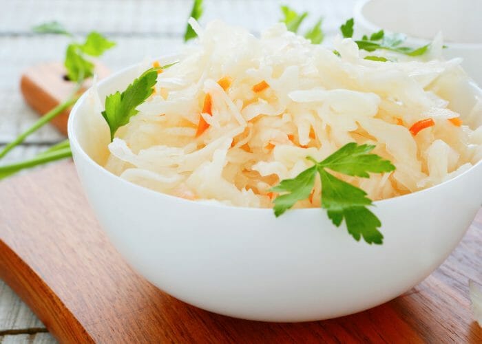 DIY sauerkraut potato salad in a white bowl on top of a wooden serving board