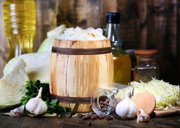 Freshly made sauerkraut in a small wooden barrel with ingredients like garlic, cabbage, oil, and spices around it on the wooden table
