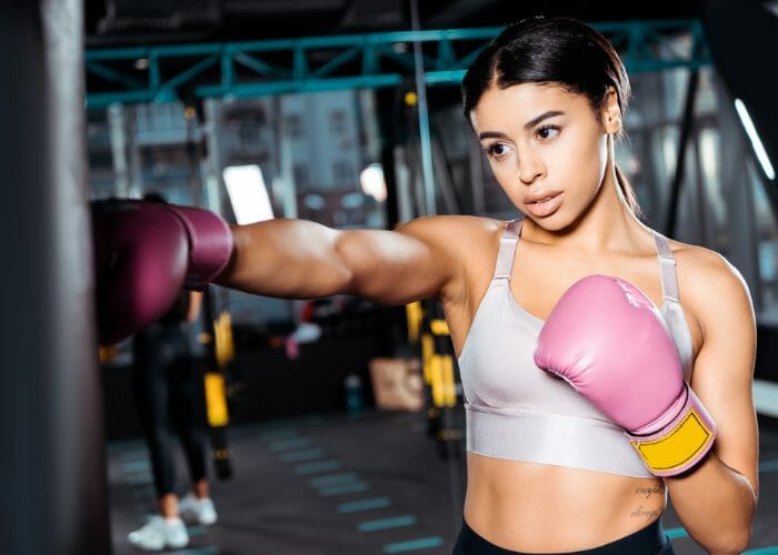 Young woman with pink boxing gloves in a gym practicing american kickboxing