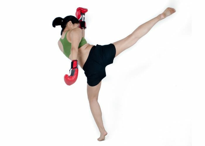 Asian woman with boxing gloves doing high side kick practicing Muay Thai kickboxing