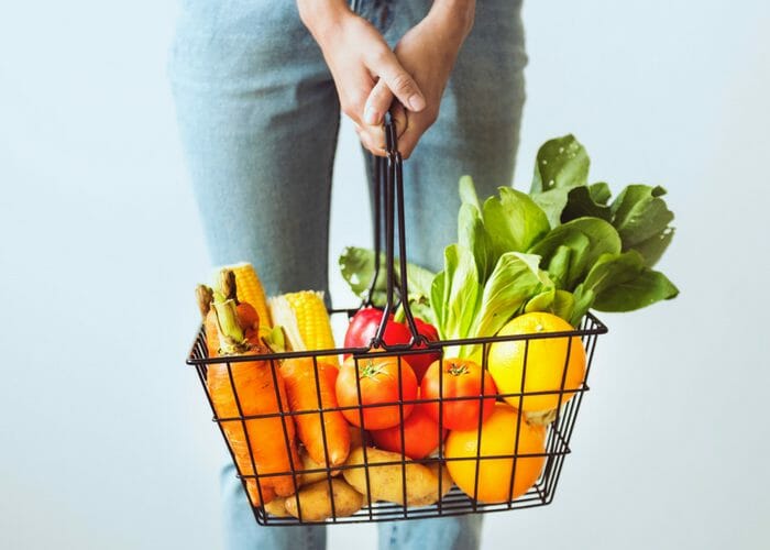 woman holding a shopping basket filled with fresh vegetables