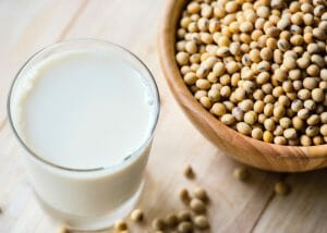 a glass of soy milk next to a bowl of soy beans