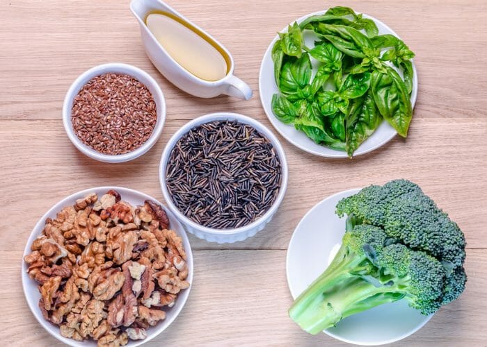 Flatlay of plant-based ingredients such as grains, olive oil, walnuts, broccoli, and green vegetables on a wooden table