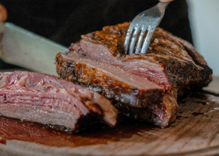 Close up of someone cutting into a juicy steak on a wooden board with a fork and knife