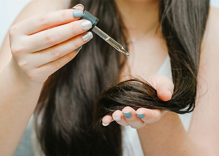 Long-haired woman using a dropper to apply citrus essential oil to her hair