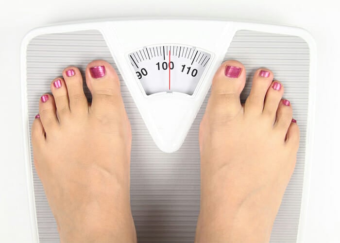 Close up of a woman's feet standing on a bathroom scale which weighs her in at over 100 kg
