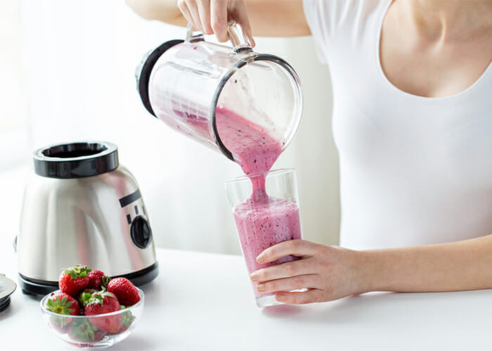 Woman pouring a freshly-blended strawberry keto protein shake into a glass