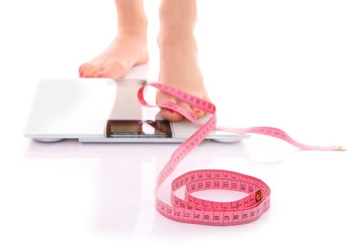 Woman on keto plateau using weight scale and measuring tape