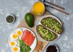 A healthy breakfast with avocados, orange juice, hard boiled eggs, salmon, nuts