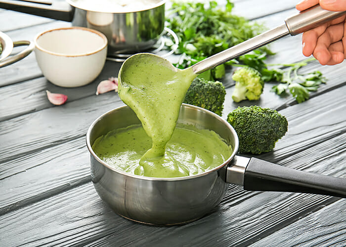 Woman mixing homemade keto broccoli and chedddar soup with a ladle