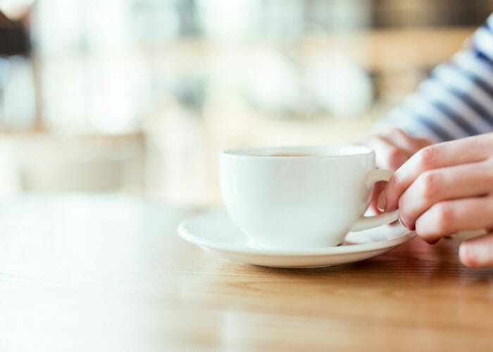woman's hand holding a coffee mug at a table