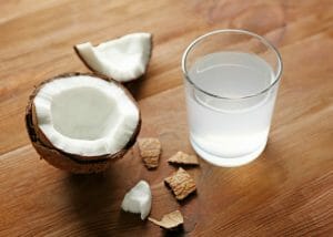 a glass of coconut water and half an open coconut on a table