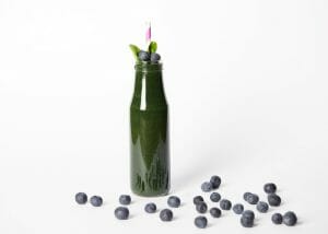 dark green smoothie in a tall bottle with a straw and blueberries 