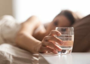 woman in bed reaching for a glass of water