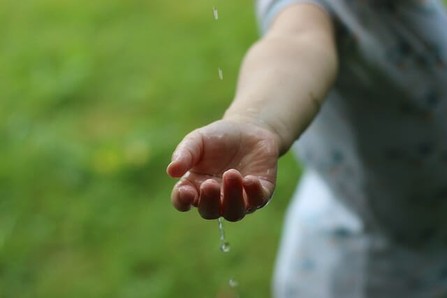 close up of a man's arm and hand being stretched ot with water drops running through his fingers. The background is green grass.