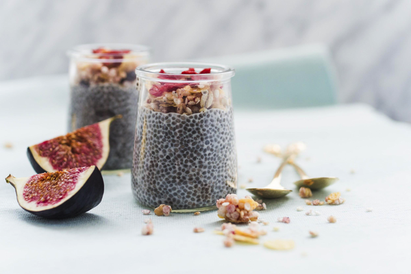 2 pots of chia see pudding topped with nuts and figs set against a white background