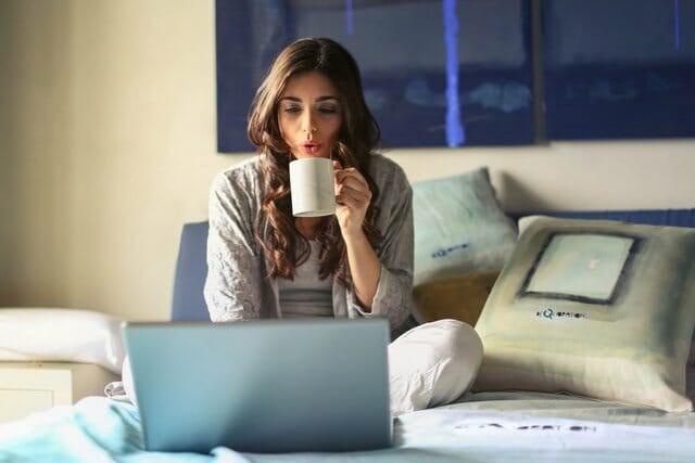 woman sat n front of an open laptop drinkng a cup of coffee and trying to take the stress out of balancing her professional and family life
