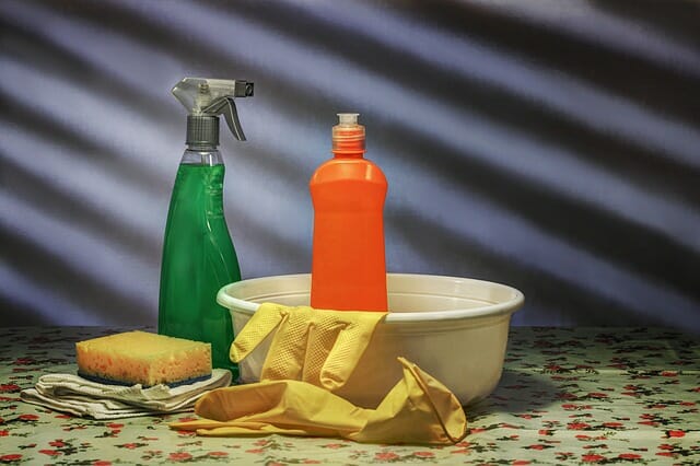 selection of cleaning materials on a table - including yellow rubber gloves, a green spray bottle, an orange squirty bottle and a sponge