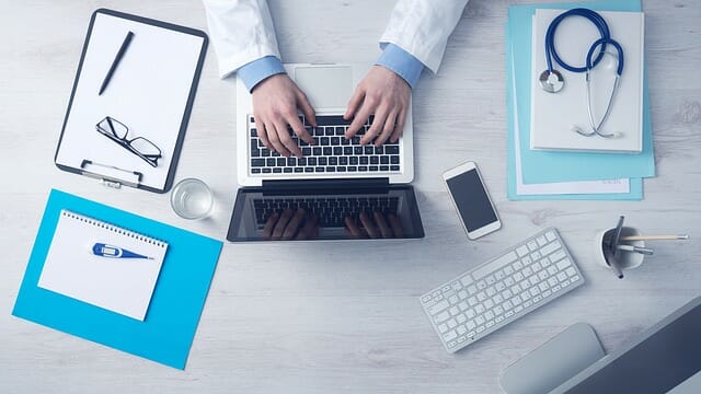 doctors hands using a laptop on a desk with other medical admin files